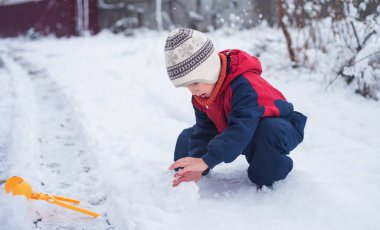 Bebek elleriyle büyük bir kartopu yaratıyor. Sıcak tulumlu kötü kalpli çocuk karla oynuyor.