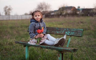 Kız bahar gecesinde eski ahşap bir bankta tek başına oturur. Avrupa baharı. Kırmızı laleli kız