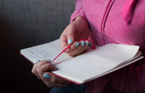 The pink book in the hands of a girl. Hands of a girl with a stylish manicure. Woman holds open notebook for records