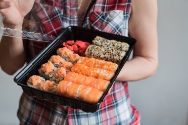 Lezzetli bir suşi seti bir kızın ellerinde. Lezzetli balıklar. Japon mutfağı. Eve restoran yemeği getirme fikri.