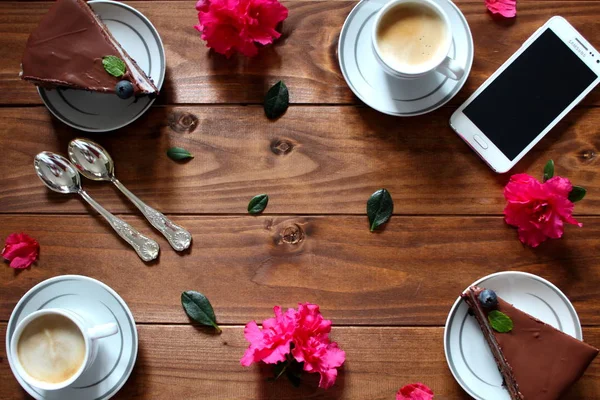 Cell phone, cake, coffee and flowers on the wooden table. Mothers Day, wedding concept with copy space. Top view.