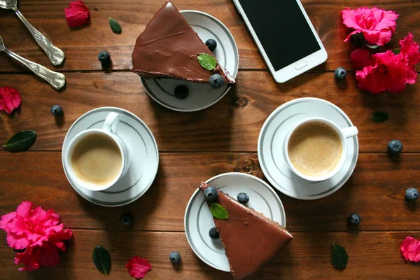 Cell phone, cake, coffee and flowers on the wooden table. Valentines, Mothers Day, wedding concept with copy space.