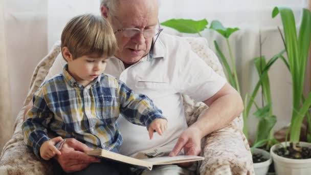 Menino lendo um livro com seu avô — Vídeo de Stock