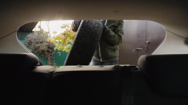 Un hombre pone neumáticos de invierno en el maletero de un coche — Vídeo de stock