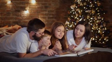 Ebeveynler ve iki çocuk yatakta yatıyor ve annem kitap okuyor.