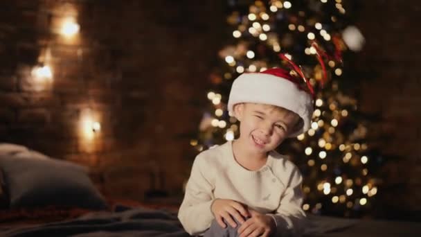 Niño vestido de Santa sombrero y sacude la cabeza — Vídeos de Stock