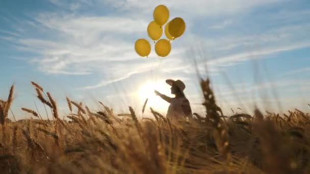 Gelukkig vrouw in rieten hoed wandelen met ballonnen in een tarweveld — Stockvideo