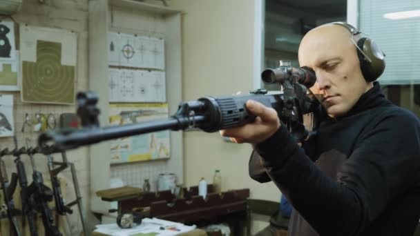 Человек в наушниках смотрит в оптический прицел снайперской винтовки — стоковое видео