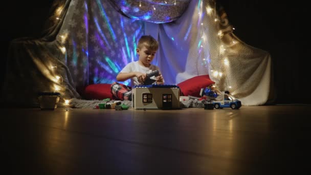 小さな男の子は家でプラスチック製のコンストラクターと遊ぶ — ストック動画