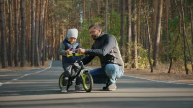 Babası küçük oğluna denge bisikleti sürmeyi öğretiyor.