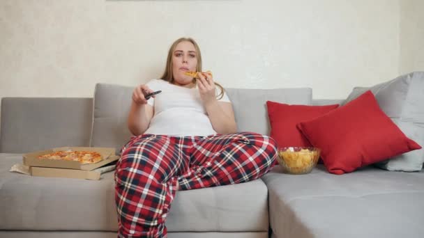 Menina com sobrepeso comer pizza e assistir tv — Vídeo de Stock