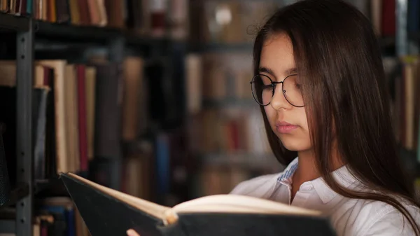 Ritratto di una giovane ragazza che legge un libro in una biblioteca — Foto Stock