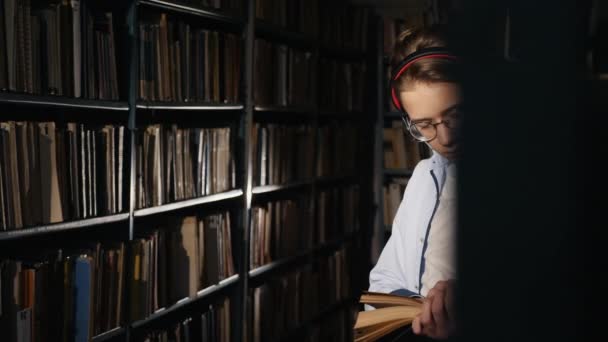 A teenager in a library reads a book in the evening — Wideo stockowe