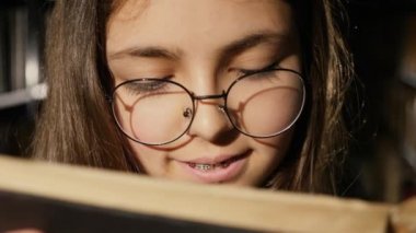 Girl with glasses reading a book in the library, close-up