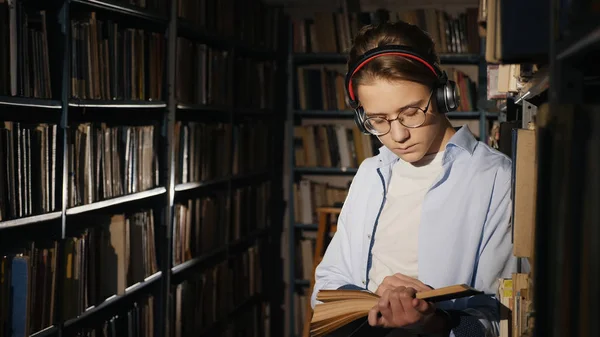 A teenager in a library reads a book in the evening