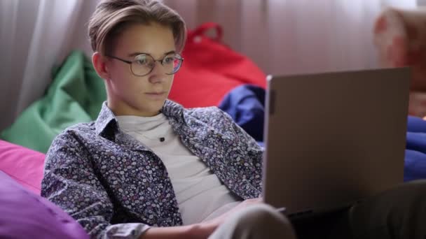 Un adolescente con estilo en gafas mirando la pantalla del ordenador portátil — Vídeos de Stock