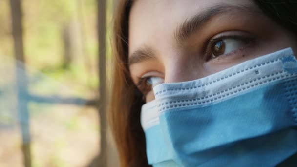 Una chica con máscara médica mira por la ventana — Vídeos de Stock