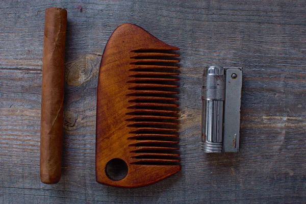 Comb for a beard, cigar, and lighter lies on a wooden background