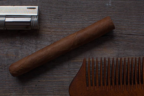 Comb for a beard, sigar, and lighter lies on a wooden background