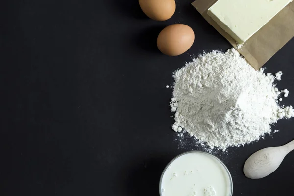 Flour, eggs, butter, sugar, milk - ingredients for dough on a black background.