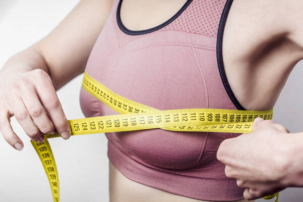 The concept of diet, weight loss. Closeup of young woman measures her breast with a measuring tape.