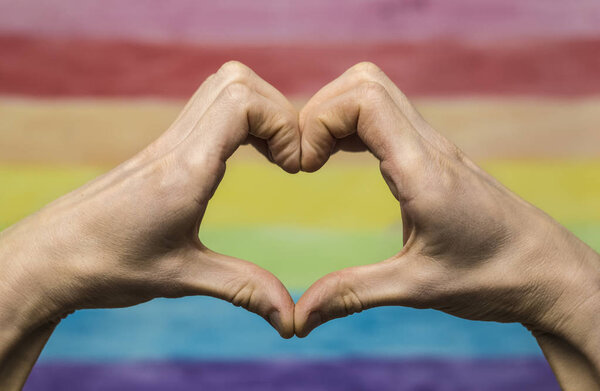 Руки делают знак сердца на фоне радужного флага. Концепция ЛГБТ
