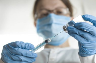 Bir şırınga ve tıbbi bir işçinin arka plan karşı bir enjeksiyon çözüm ile bir şişe. Doktor bir şırınga aşı ile tutuyor. Sıvı ilaç veya ilaç.