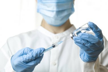 Bir şırınga ve tıbbi bir işçinin arka plan karşı bir enjeksiyon çözüm ile bir şişe. Doktor bir şırınga aşı ile tutuyor. Sıvı ilaç veya ilaç.