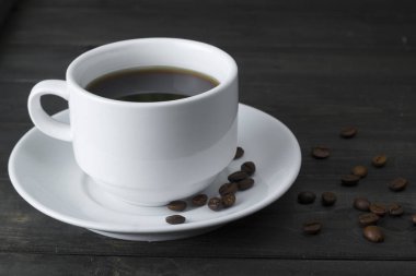 Bir fincan kahve, koyu ahşap tahta üzerinde kahve çekirdekleri.