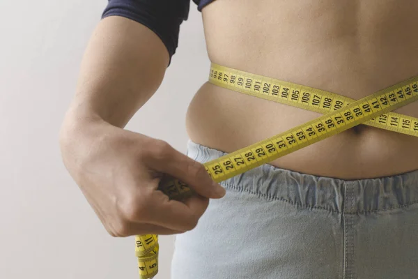 A young woman measures her waist with a measuring tape. The concept of losing weight.