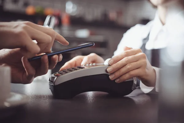 The client pays in the cafe with a smartphone using NFC technology. Contactless payment by mobile phone on a POS terminal.