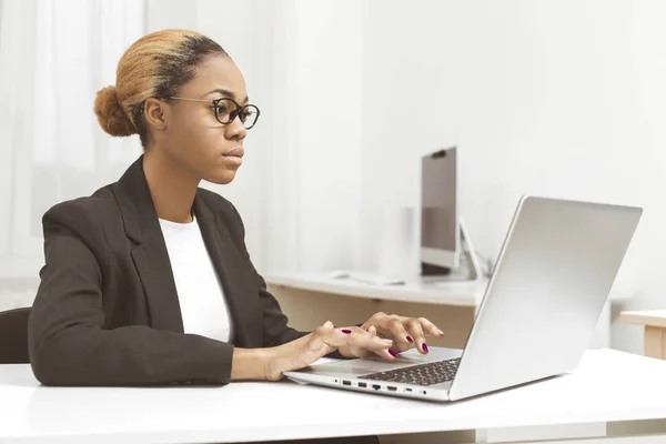 Business African American young woman working in office at laptop. Black girl manager uses a computer in the workplace.