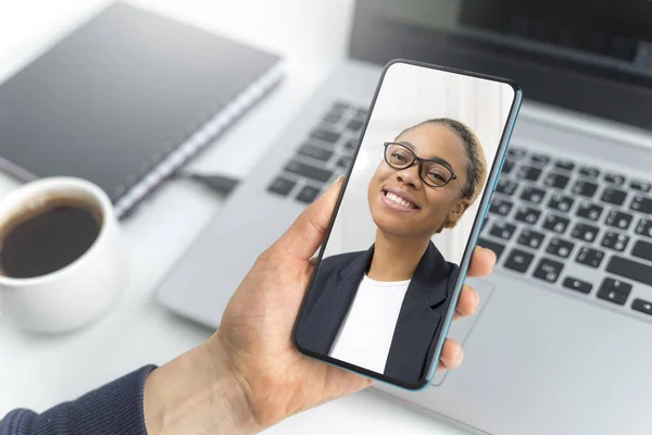 Video online chat talks on smartphone screen with african american business woman. Hands holding a mobile phone for a video conference.
