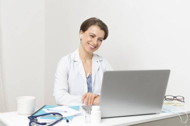 Gülümseyen bir kadın doktorun portresi hastaya bilgisayar ekranında görüntülü konuşma öneriyor. Doktor konferanstaki müşteriyle bağlantı kurar, bilgisayardaki web kamerasıyla konuşur..