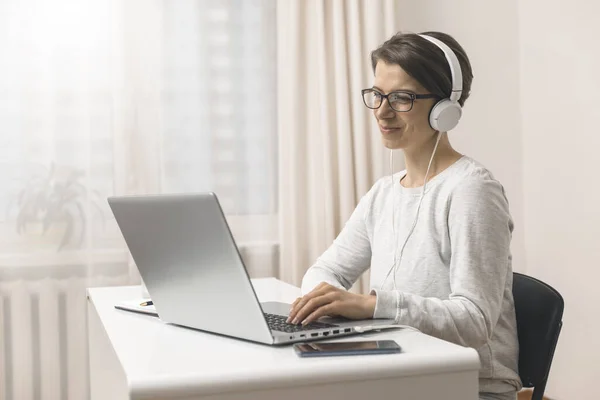 Female freelancer works on a remote house. A woman is studying online video chat on a laptop. Girl in headphones communicates by video call.