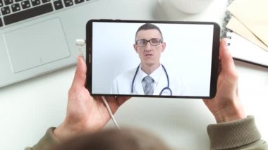 Doktor, tablet ekranında çevrimiçi bir sohbete girmenizi tavsiye ediyor. Bir erkek doktorla bir hastanın uzaktan bağlantısı. Video konferansı ile tıbbi yardım.