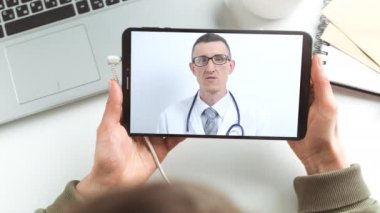 Doktor, tablet ekranında çevrimiçi bir sohbete girmenizi tavsiye ediyor. Bir erkek doktorla bir hastanın uzaktan bağlantısı. Video konferansı ile tıbbi yardım.