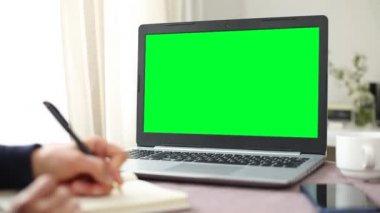 Yeşil ekran laptop monitörü. Boş alan, maket yap. Öğrenci bir deftere notlar yazar.. 