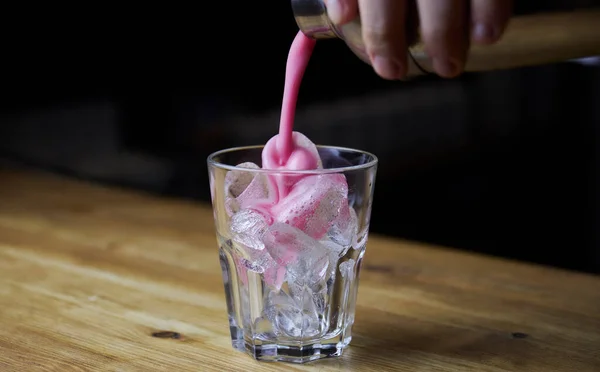 Bartender pouring strong alcoholic drink into small glasses on bar. Red shots at the nightclub. Red alcoholic drink in glasses on bar. Red cocktail at the nightclub. Barman preparing cocktail shooter