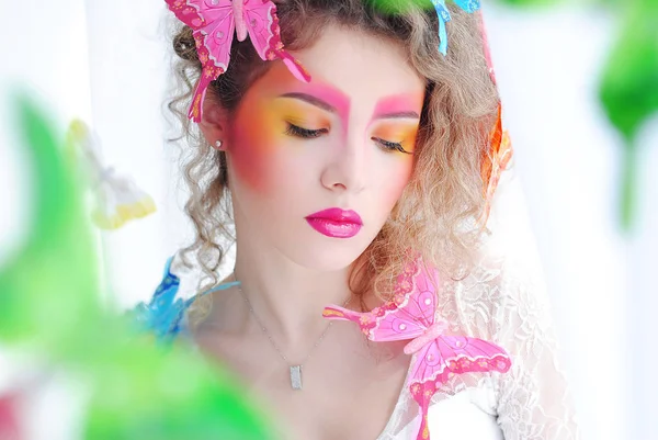 Bright makeup of the girl on her face. Portrait of a girl on a white background. Butterflies in the hair of the model. Makeup and cosmetics.