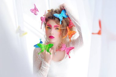 Yüzünde makyaj parlak kız. Pencerenin yanındaki Bayan. Beyaz zemin üzerinde bir kız portresi. Saç modelinin kelebekler. Makyaj ve kozmetik.