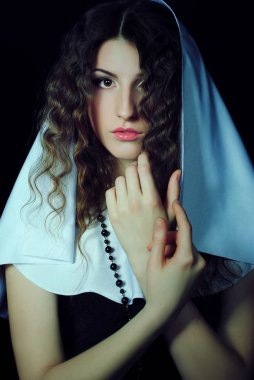 Kızın yüzü parlak makyaj. Güzel bir rahibe bir haç ile. Siyah bir arka plan bir kadın portresi. Makyaj ve kozmetik.