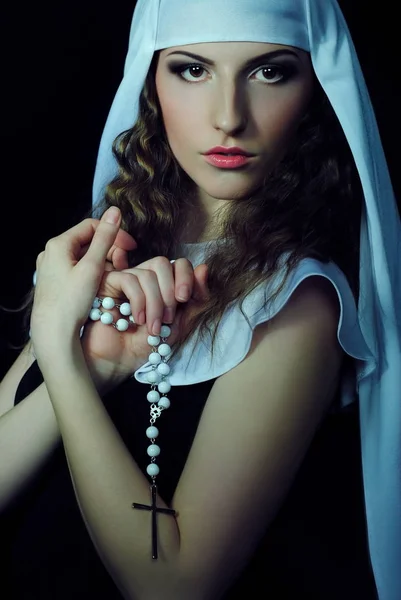 Bright makeup on the girl\'s face. A beautiful nun with a cross. Portrait of a lady on a black background. Makeup and cosmetics.