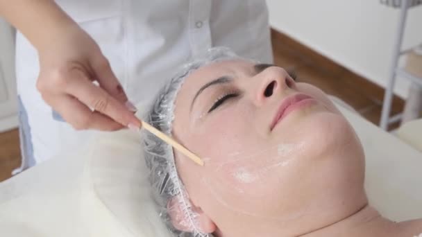 若い女性美容師は女性患者の顔に化粧品を適用します スパ化粧品の手順 — ストック動画
