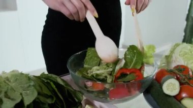 Genç bir kadın sebze salatasını karıştırıyor. Beyaz modern mutfak. Sebze, domates, kırmızı biber, marul, salatalık, avokado, limon. 4k