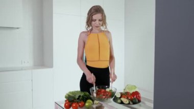 Kadın sebze salatasına limon suyu sıkıyor. Beyaz modern mutfak. Sebze, domates, kırmızı biber, marul, salatalık, avokado, limon. 4k