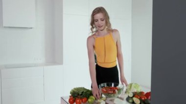  Genç bir kadın sebze salatasına limon suyu sıkıyor. Beyaz modern mutfak. Sebze, domates, kırmızı biber, marul, salatalık, avokado, limon. 4k