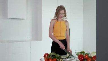  Sebze salatası için salatalık doğrayan genç bir kadın. Beyaz modern mutfak. Sebze, domates, kırmızı biber, marul, salatalık, avokado. 4k