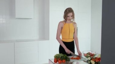 Sebze salatası için kırmızı biber dilimleyen genç bir kadın. Beyaz modern mutfak. Sebze, domates, kırmızı biber, marul, salatalık, avokado. 4k