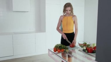 Sebze salatası için kırmızı biber dilimleyen genç bir kadın. Beyaz modern mutfak. Sebze, domates, kırmızı biber, marul, salatalık, avokado. 4k